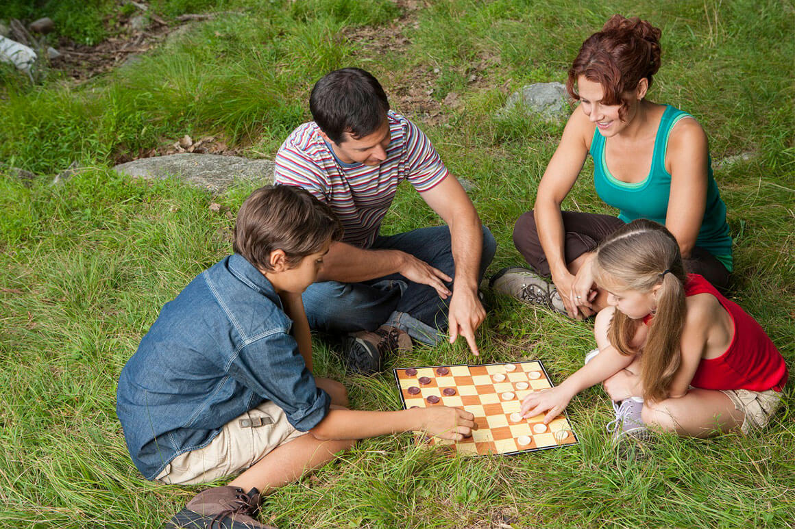 Mom, dad, and two kids playing checker on the grass
