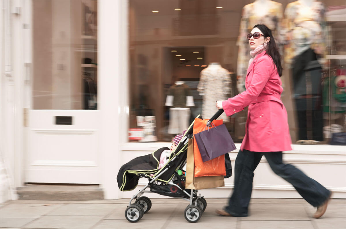 Woman carrying shopping bags and pushing a stroller.