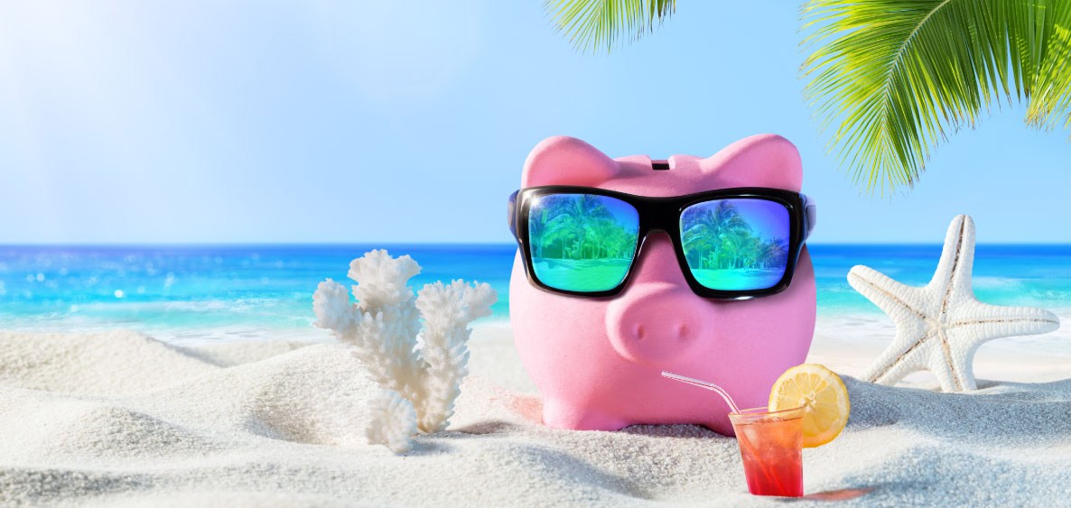 Pink piggy bank with sunglasses on at the beach with a tropical drink