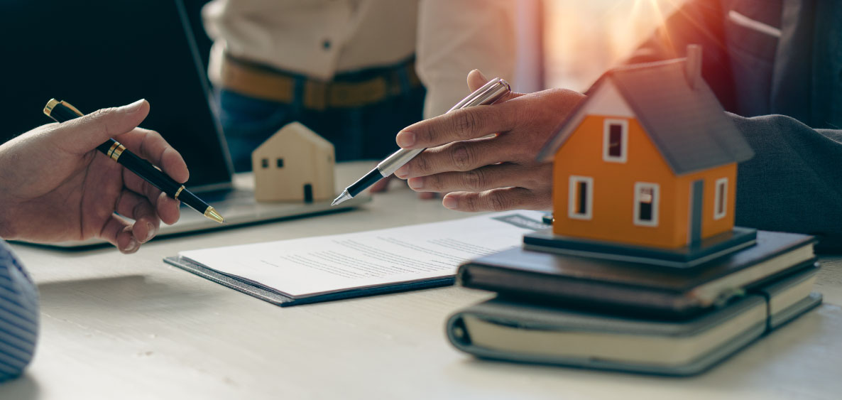 Hands holding pens with a house model on notebooks.