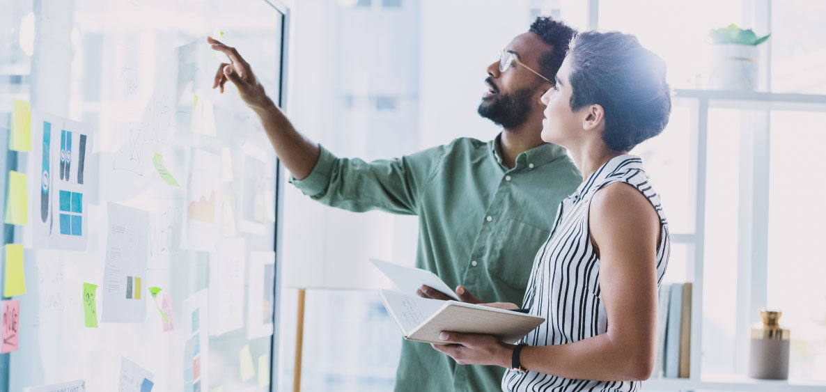 Man pointing at a board while woman hold a book.