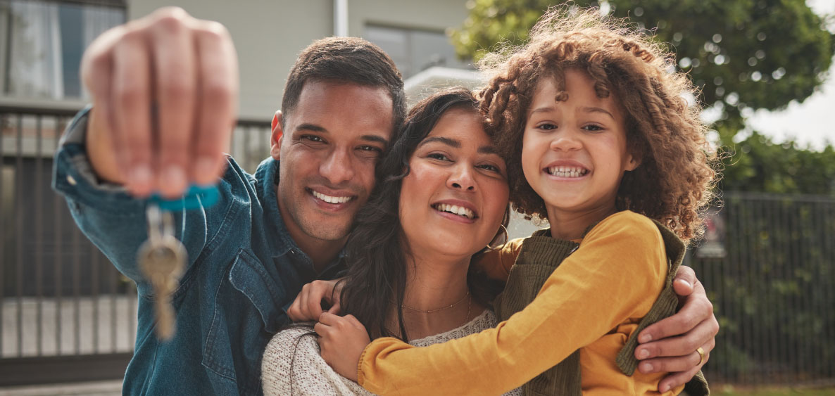 Husband, wife, and child together with husband holding a key in front of a house.