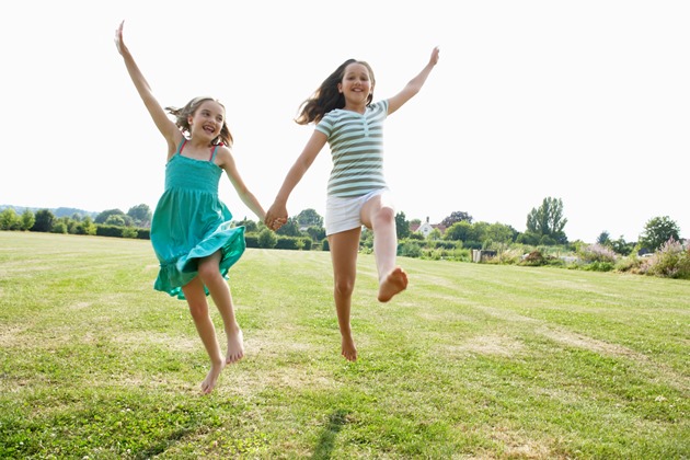 Two girls holding hands jumping on the grass