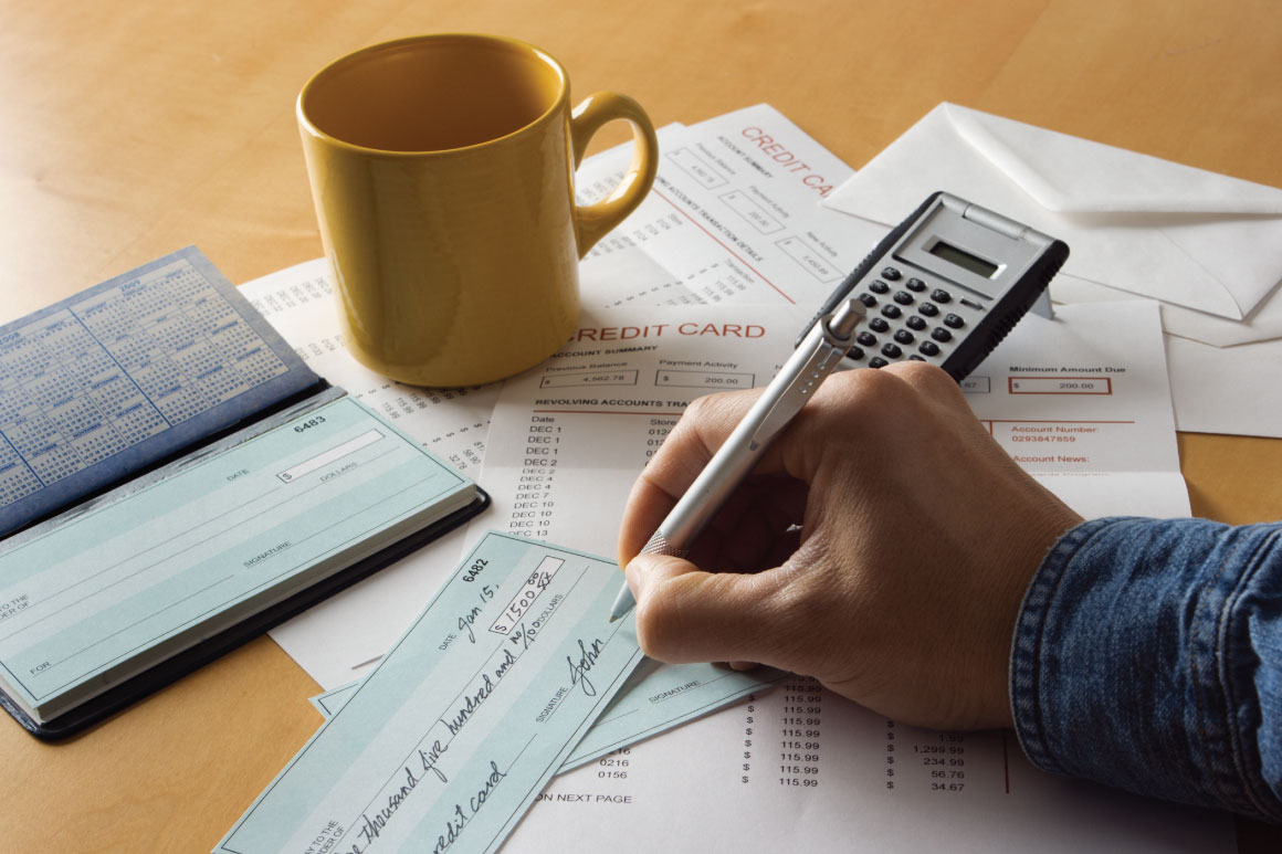 Hand writing a check with checkbook and coffee mug closeby