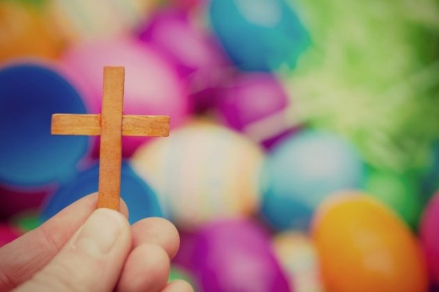 Hand holding a cross with Easter eggs in the back