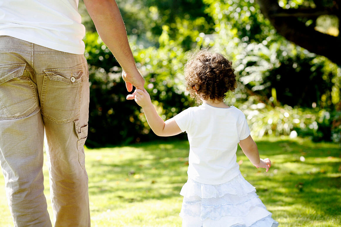 Father holding young daughter's hand while walking