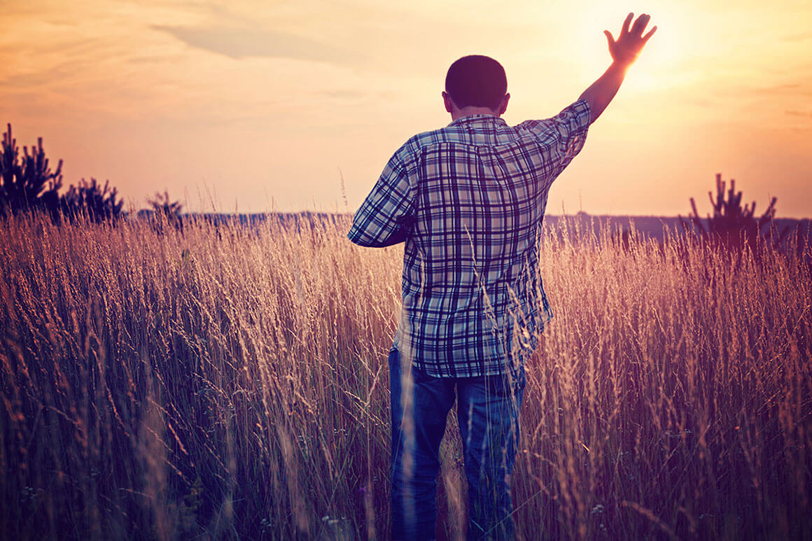 Man standing in the field raising his hand up to heaven