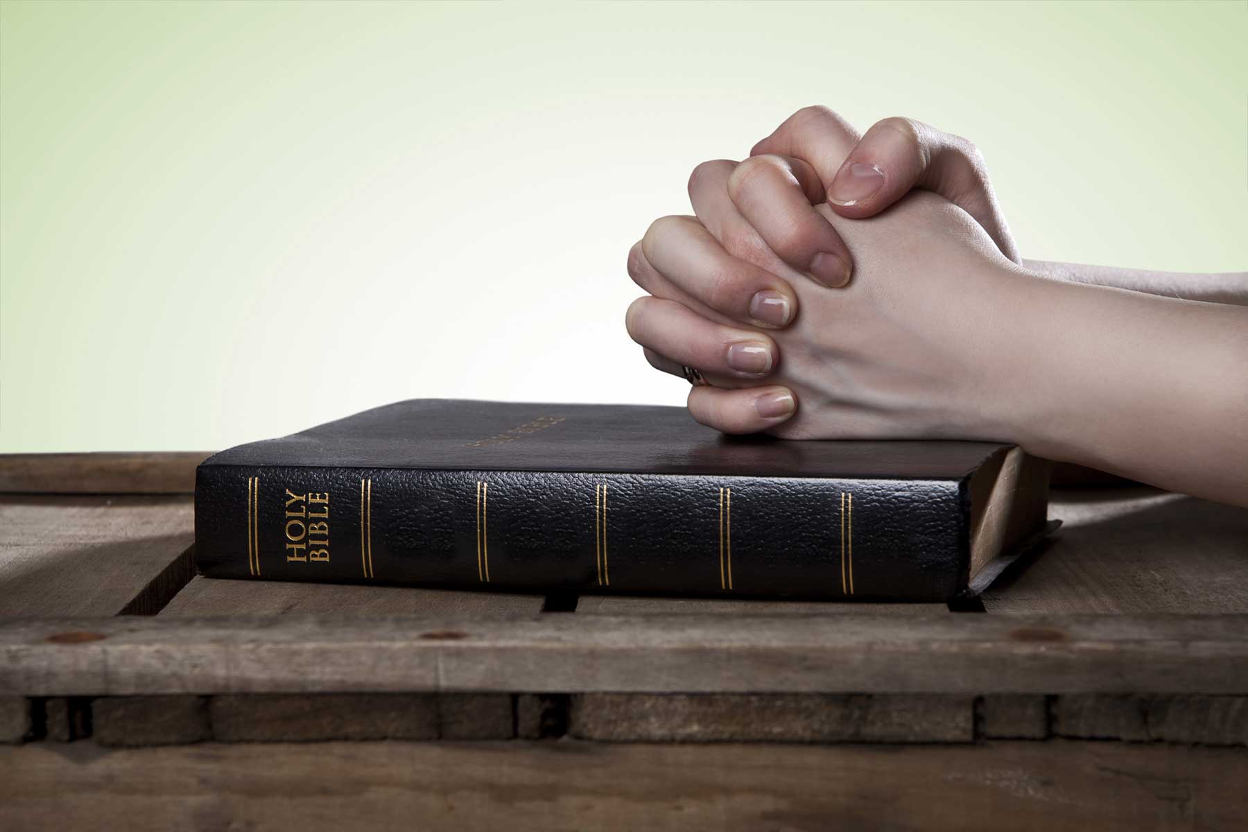 Hands praying on the Bible