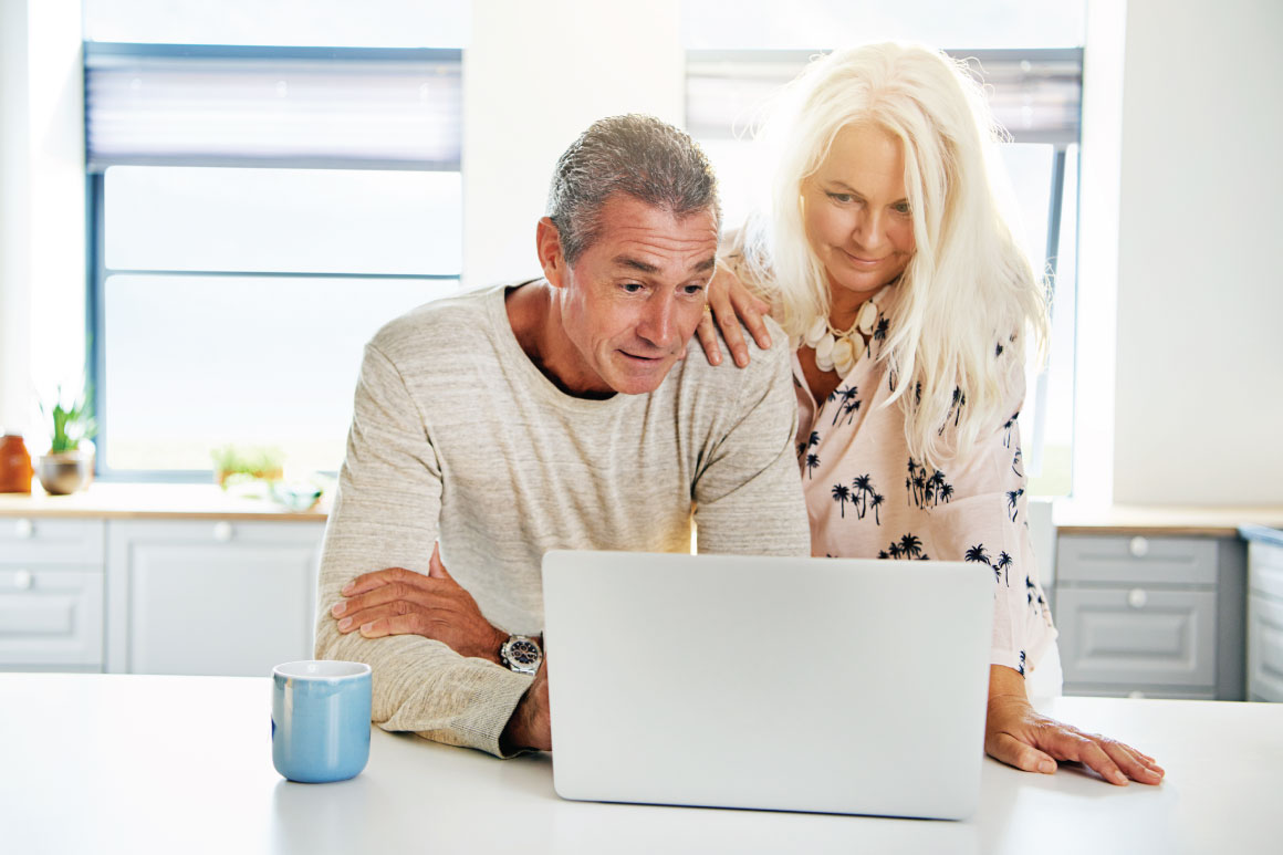 Husband and wife looking at their laptop together on their kitchen counter