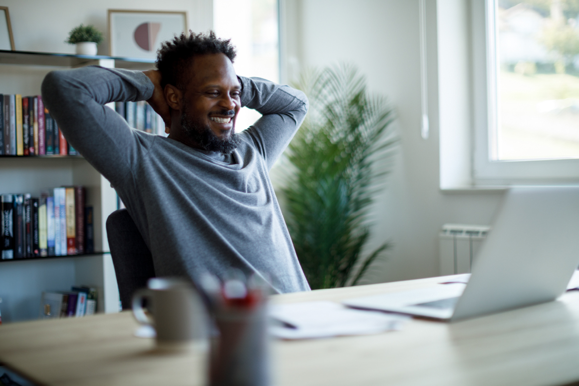 Happy man sitting at his desk in front of his laptop