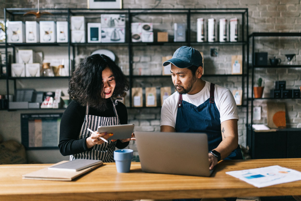 Man and woman in aprons working together while on their electronic devices.