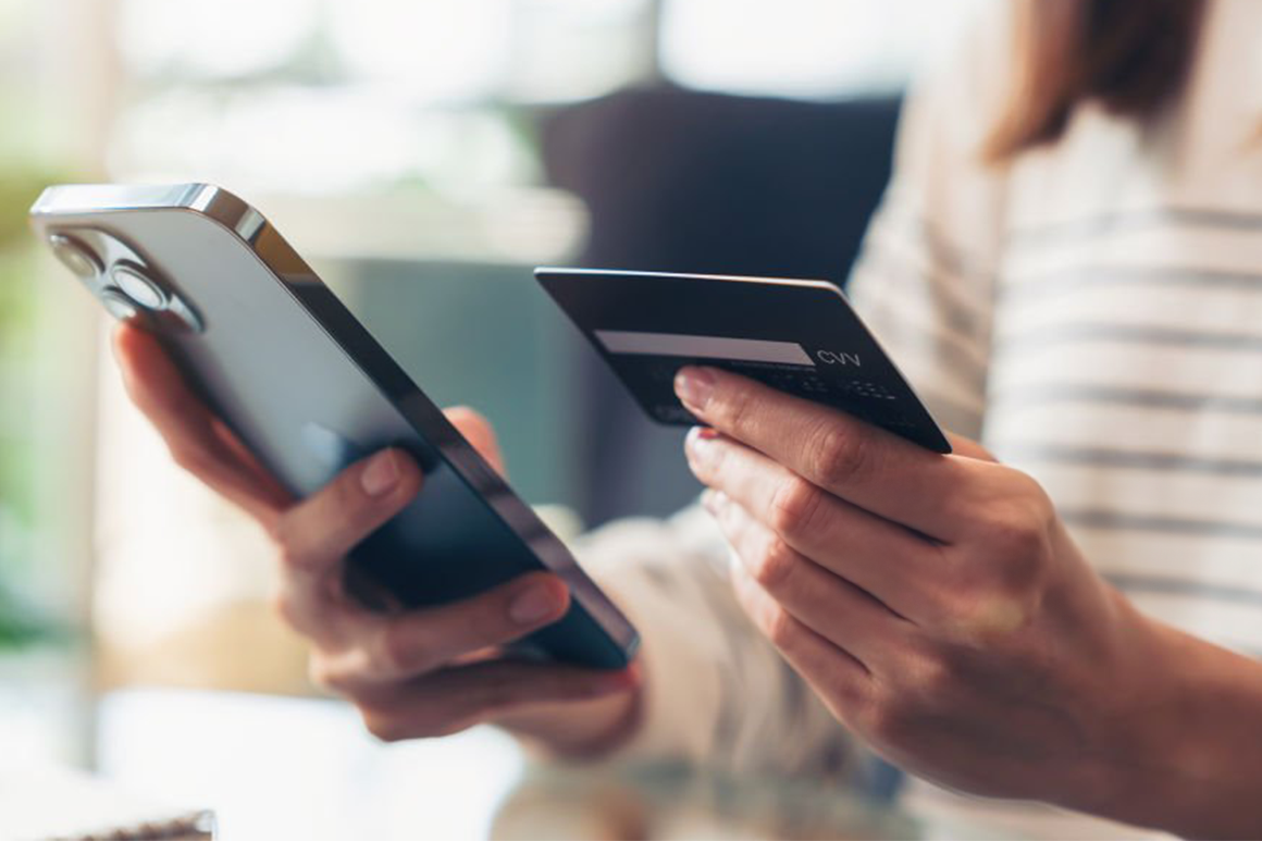 One hand holding a mobile phone and the other holding a credit card
