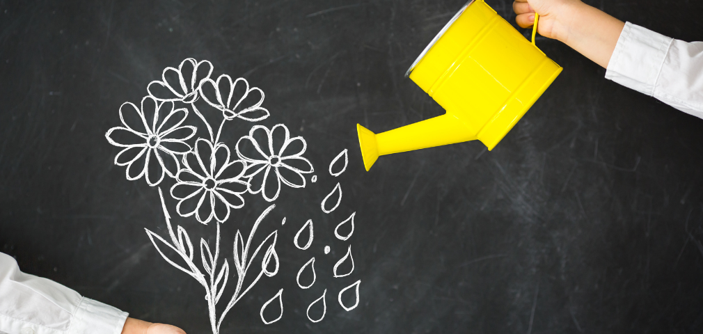 Yellow watering held over a chalkboard with chalked flowers and water