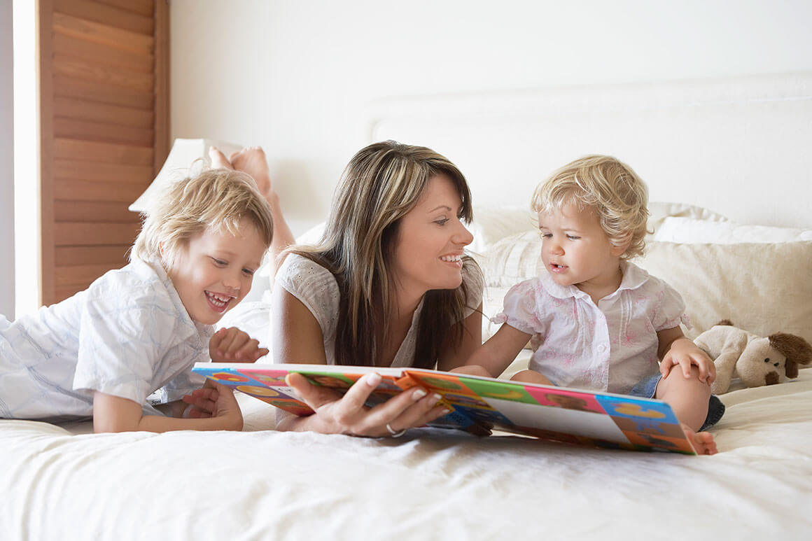 Mother reading on the bed with her two babies