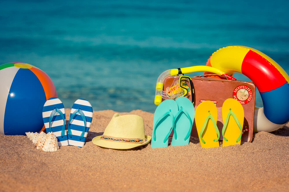 Flip flops, beach ball, floatie, and fedora hat lined up at the beach